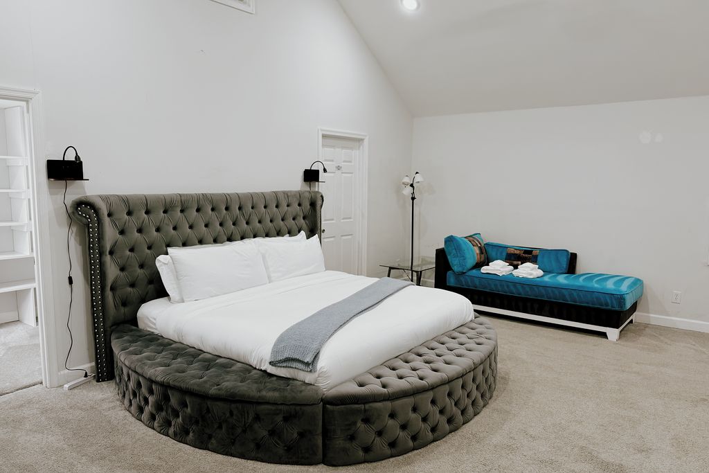 A bedroom with a round bed, a blue sofa, a lamp, and a door.