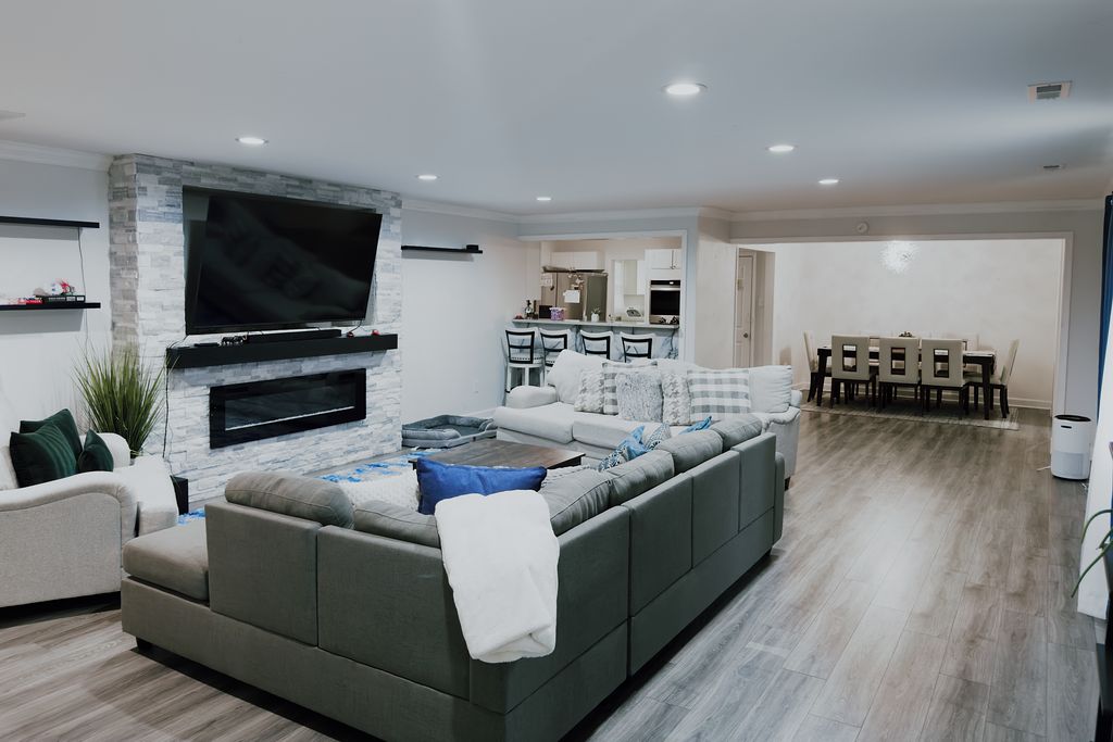 A modern living room with a large flat-screen TV, a sectional sofa, and a dining area with a table and chairs.