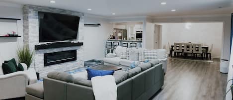 A modern living room with a large flat-screen TV, a sectional sofa, and a dining area with a table and chairs.