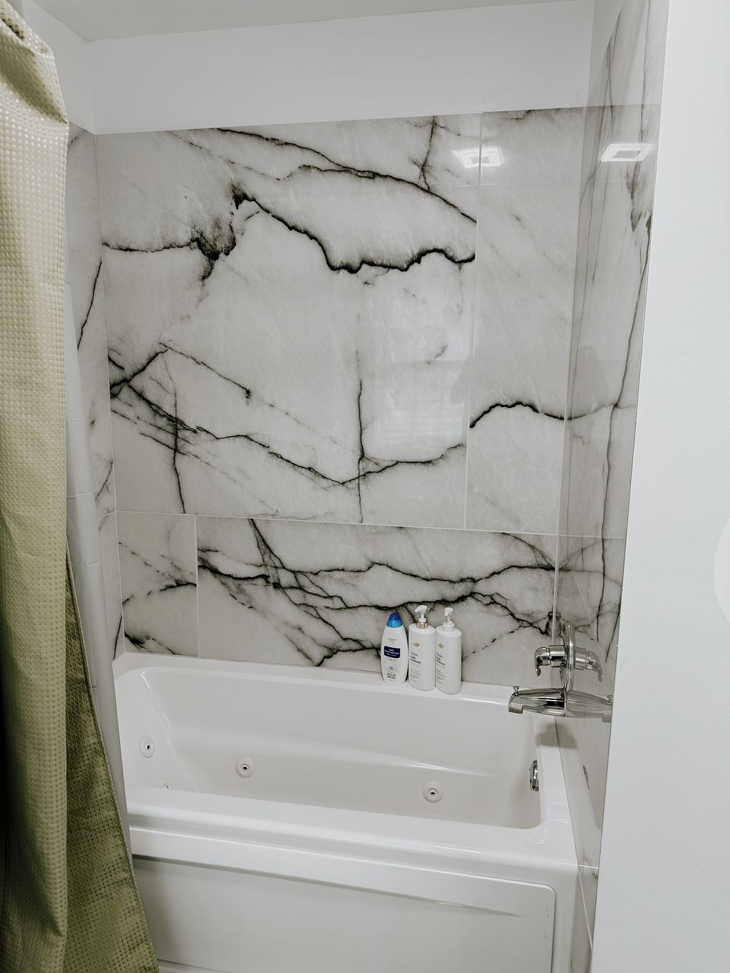 A bathroom with a marble wall, a bathtub, and toiletries on the edge.