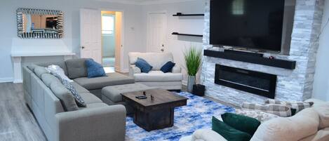 A modern living room with a sectional sofa, a fireplace, a mounted TV, and a decorative mirror.
