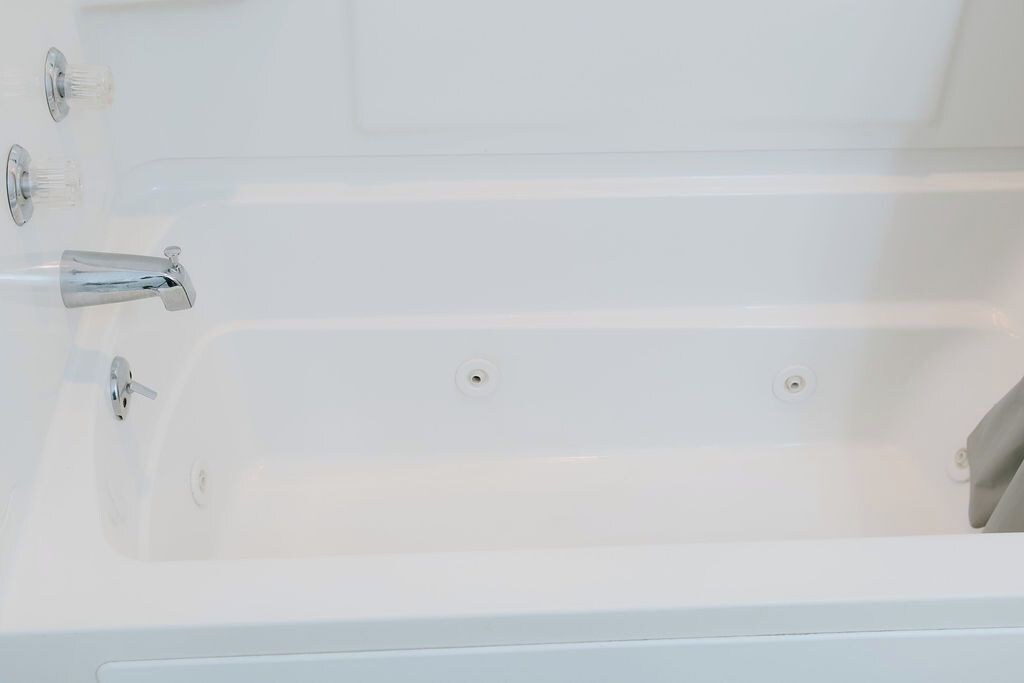 A white bathtub with two faucets and a drain.