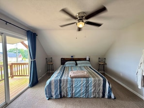 A bedroom with a ceiling fan, a bed with striped bedding, two nightstands, and a view of a deck through a sliding glass door.