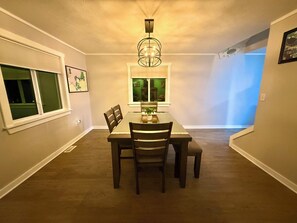 A dining room with a table, chairs, a chandelier, and a window with blinds.