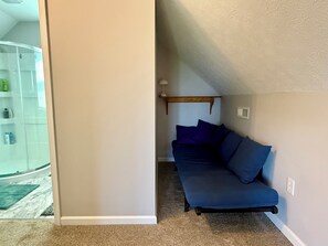 A room with a blue sofa, a wooden shelf, and a glass shower enclosure.