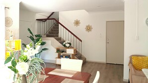 Una sala de estar con una escalera de madera, una mesa de comedor con sillas y un sillón amarillo.