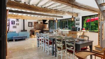Un comedor amplio con una larga mesa y sillas, una cocina al fondo y una escalera que conduce a un nivel superior.