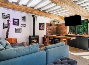Una sala de estar acogedora con chimenea, un sofá y una zona de cocina con pared de ladrillo y vigas de madera.