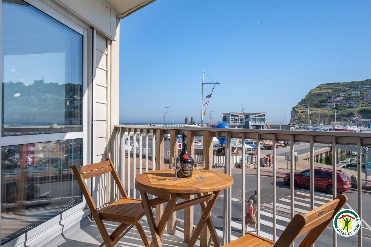 Een balkon met een tafel en stoelen, een fles champagne en uitzicht op een kustplaats met gebouwen en een vlag.