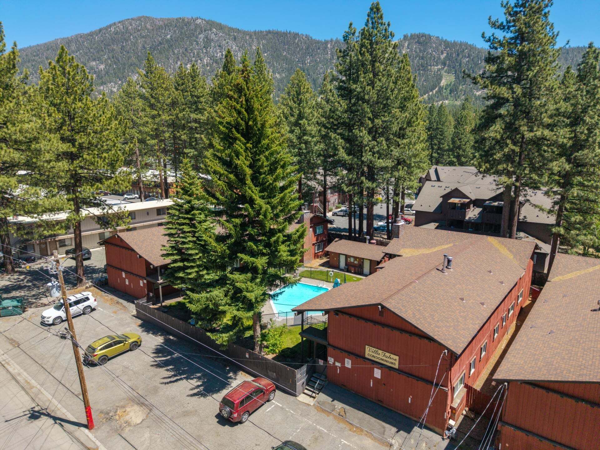 Un edificio de varios pisos con piscina, rodeado de altos árboles y un paisaje montañoso.