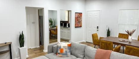 A modern living room with a sectional sofa, a dining table, and a kitchen in the background.