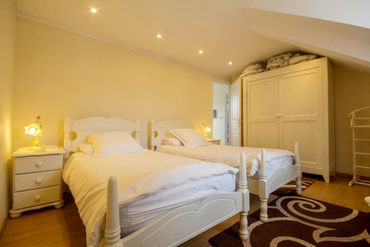 Een slaapkamer met twee bedden, een kledingkast, een nachtkastje met een lamp en een kamerkleed met een patroon.