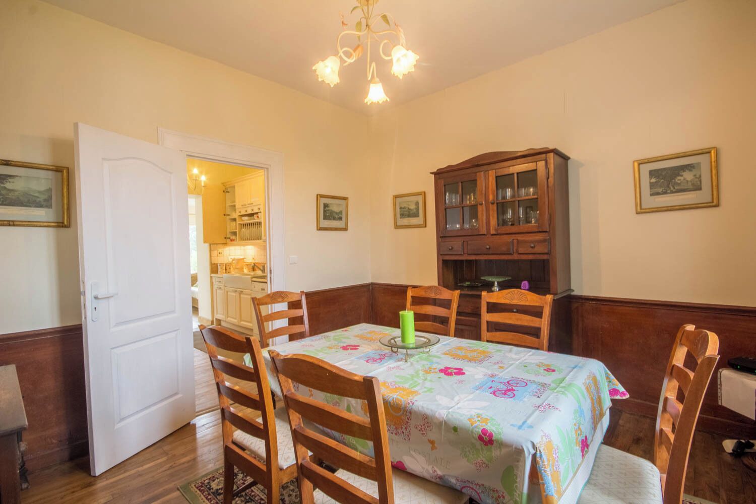 Een eetkamer met een tafel gedekt voor vier personen, houten stoelen, een kroonluchter en een kast met glazen deuren.