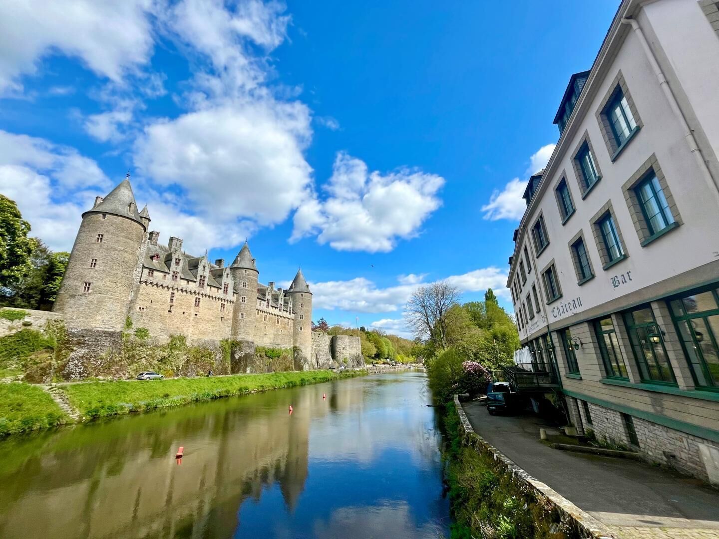 Un castillo rodeado por un foso, un río y un edificio con un cartel que dice 'Bar Chateau'.