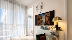 Ett modernt vardagsrum med ett soffbord i glas, en soffa, en randig pall, en lampa och en tavla på väggen.