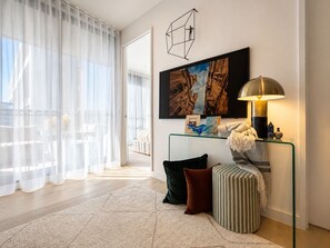 Ein modernes Wohnzimmer mit einem Glastisch, einer Couch, einem gestreiften Ottomanen, einer Lampe und einem Bild an der Wand.