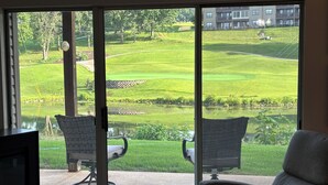 A room with a large sliding glass door leading to a patio with two chairs and a small table. - Relax & Unwind~Cozy 1bed/1bath Condo with Beautiful Pond & Golf Views (Branson)