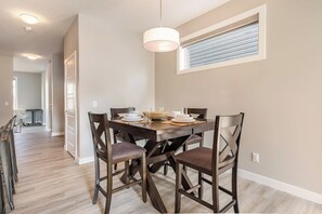 A dining area with a wooden table, chairs, and a hanging light fixture. - Green Bay Nest - 2BR, AC, Garage, Backyard, Self Checkin, Professionally Cleaned (Calgary)