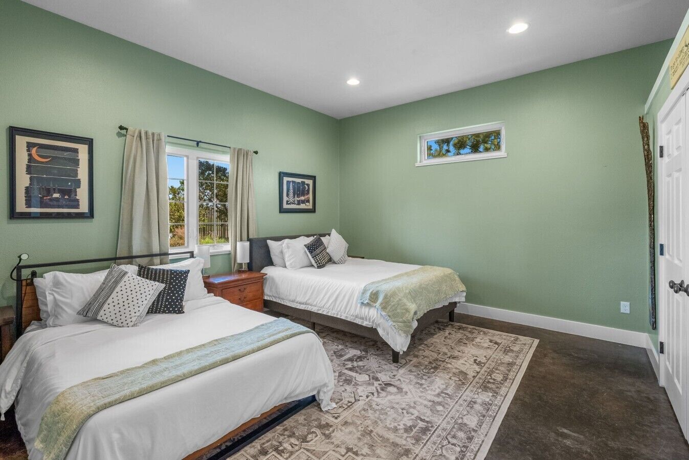 A bedroom with two beds, a window with curtains, a rug, and artwork on the walls.