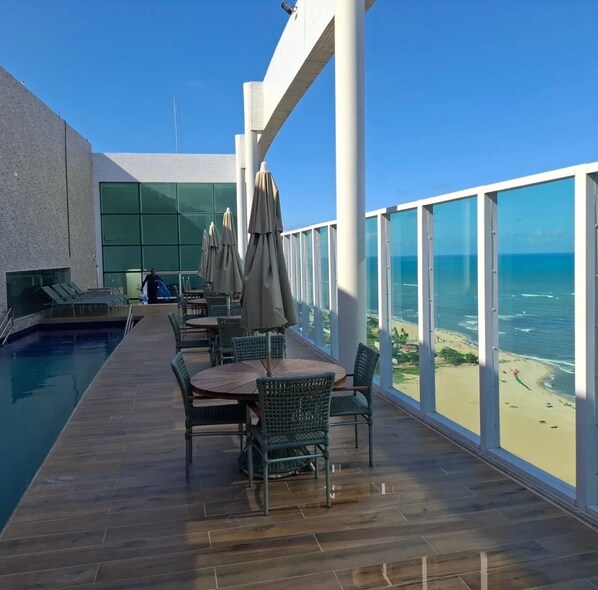Um terraço com piscina, área de estar externa e vista para a praia.