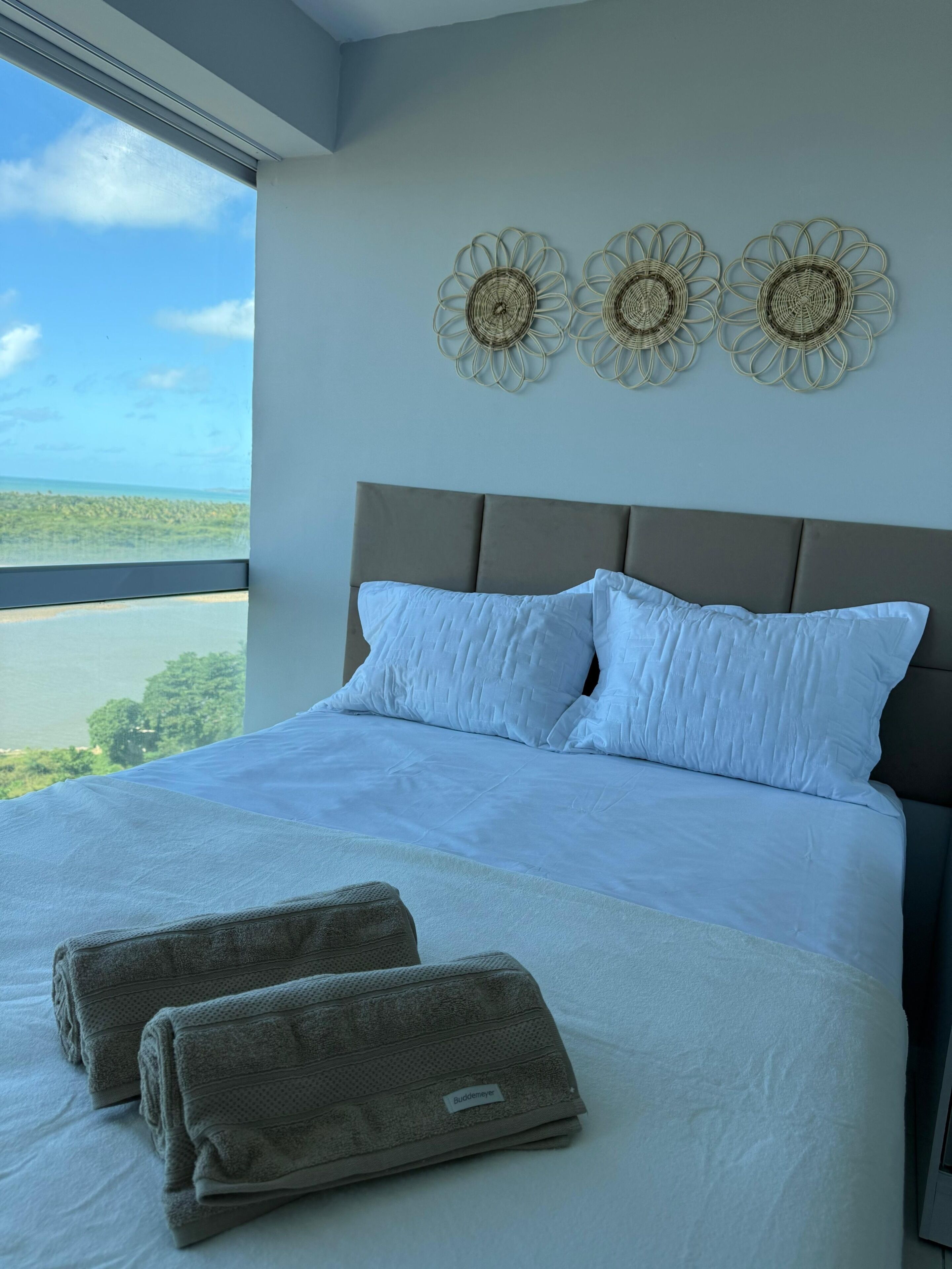 A bed with white bedding, a view of the outdoors, and three wall decor pieces.