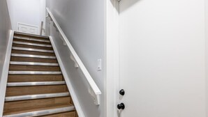 Una escalera con escalones de madera y barandas blancas que conduce a una puerta blanca con picaporte negro.