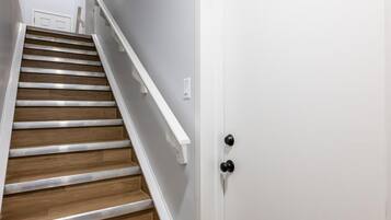 A staircase with wooden steps and white railings, leading to a white door with a black handle.