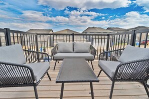 A deck with outdoor furniture, including a sofa and chairs, overlooking a residential area. - The Emerald - 3BR with King Beds |  BBQ | AC | Full-Kitchen | Laundry (Calgary)