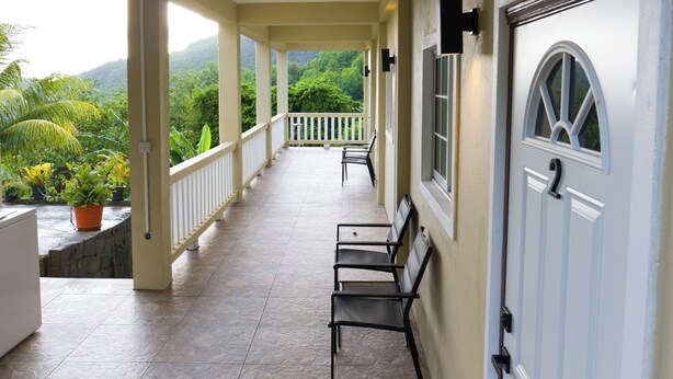 A covered porch with a view of greenery, a white door, and a bench. - Green Valley Luxe | Modern Studio Style Apartment with Verandah (Kingstown)