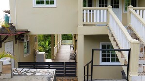 A two-story building with a balcony, a staircase, and a covered outdoor area with seating. - Green Valley Luxe | Modern Studio Style Apartment with Verandah (Kingstown)