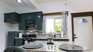 A kitchen with dark green cabinets, a microwave, a stove, and a sink. There are two plates on the counter. - Green Valley Luxe | Modern Studio Style Apartment with Verandah (Kingstown)