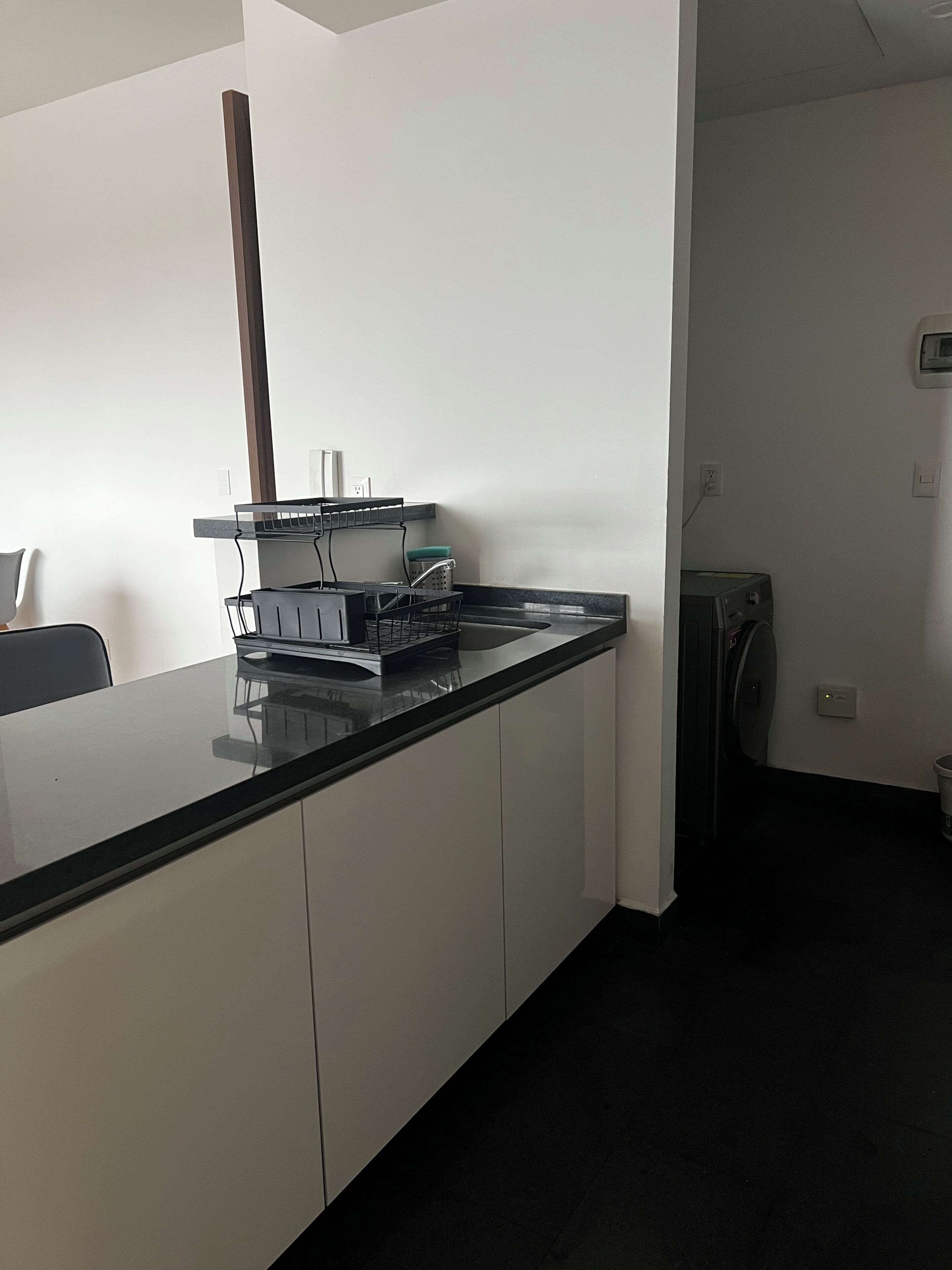 A kitchen with a black countertop, white cabinets, a sink, and a microwave.