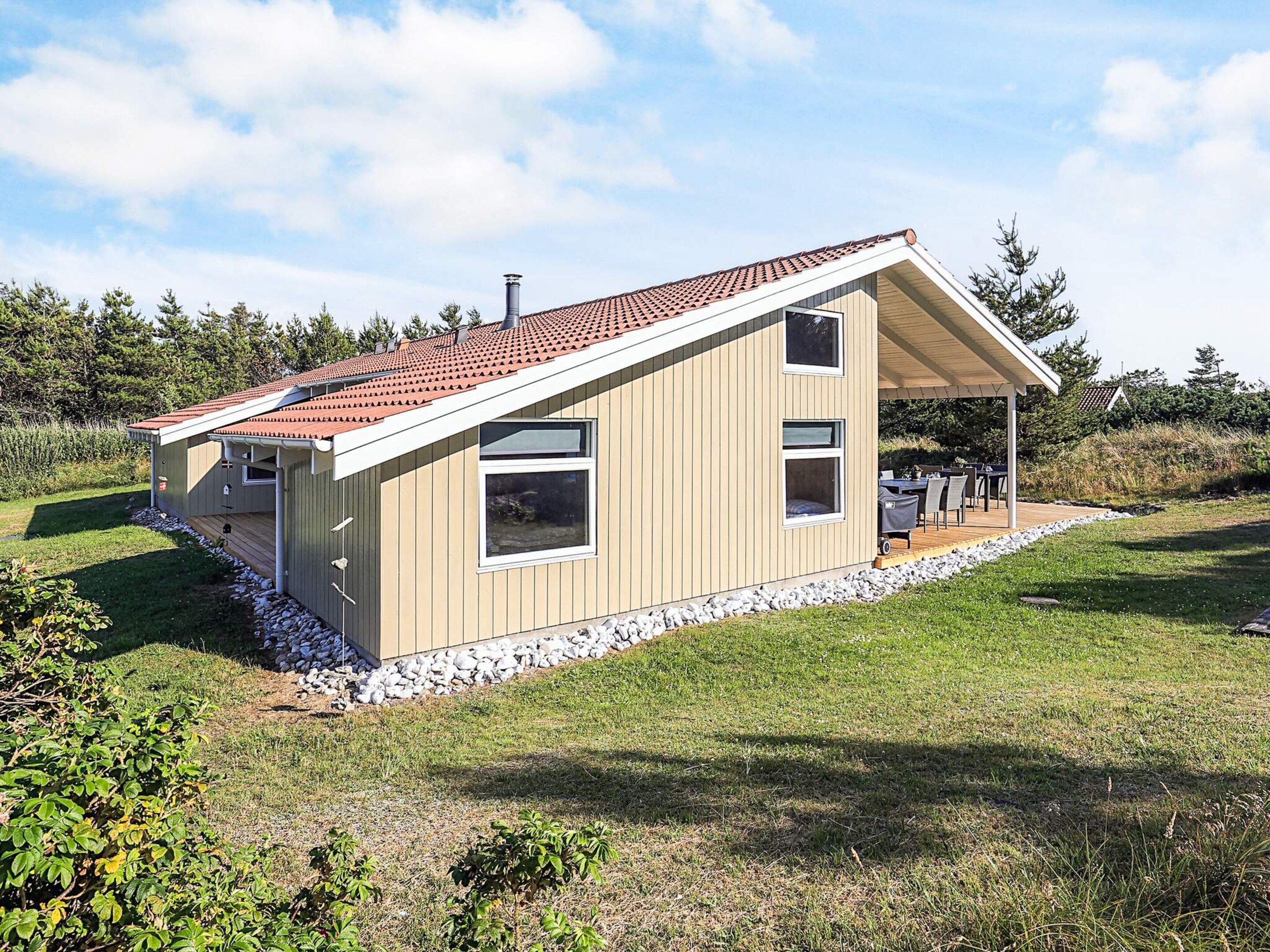 A modern single-story house with a sloped roof, a covered patio, and a stone foundation.