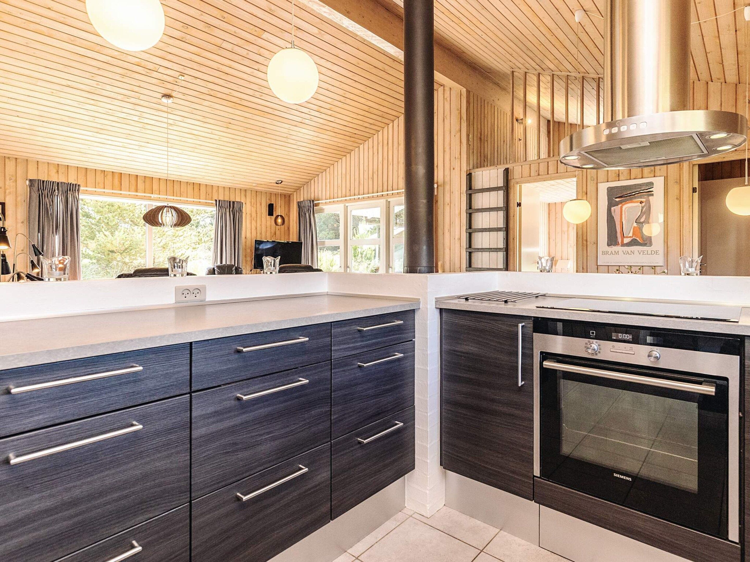 A modern kitchen with dark cabinetry, a stainless steel oven, and a large window.