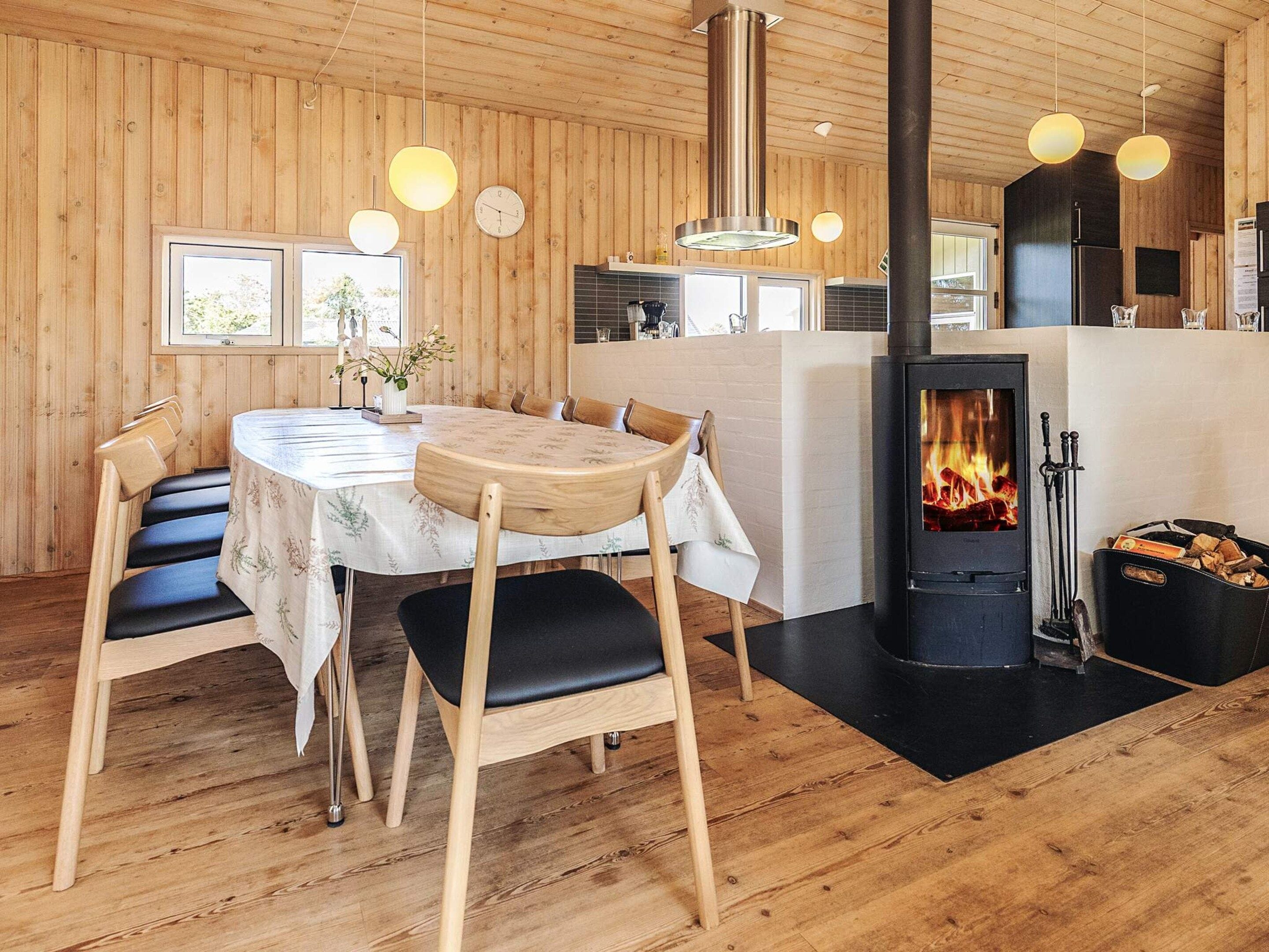 A cozy room with a wooden interior, a round dining table with chairs, a built-in stove, and a window with a view.