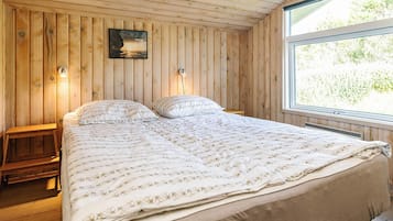 Et soveværelse med træpaneler, seng, to sengeborde, en lampe på hvert bord, et vindue og et billede i ramme på væggen.