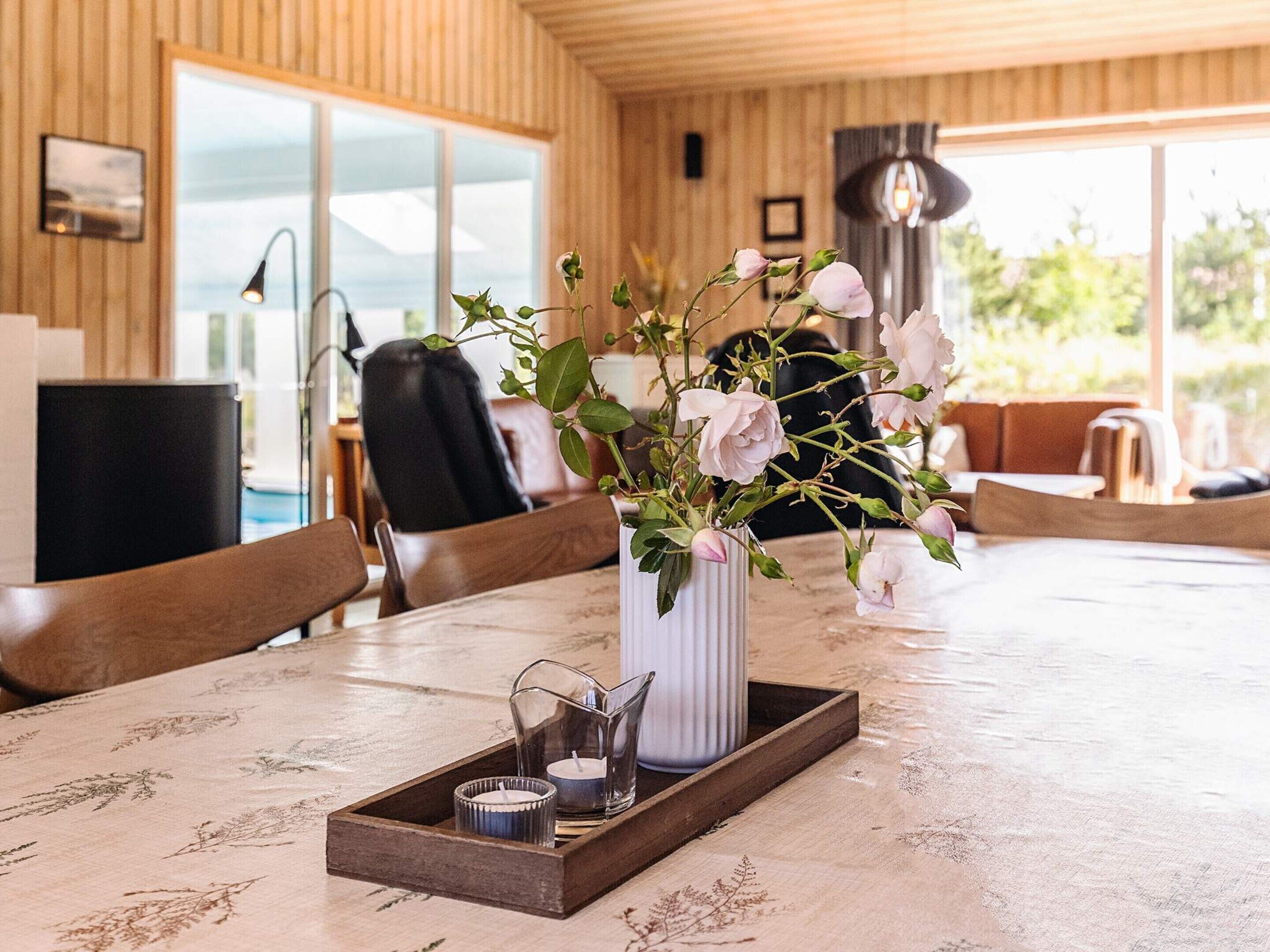 A wooden interior with a dining table, chairs, a vase with flowers, and candles.