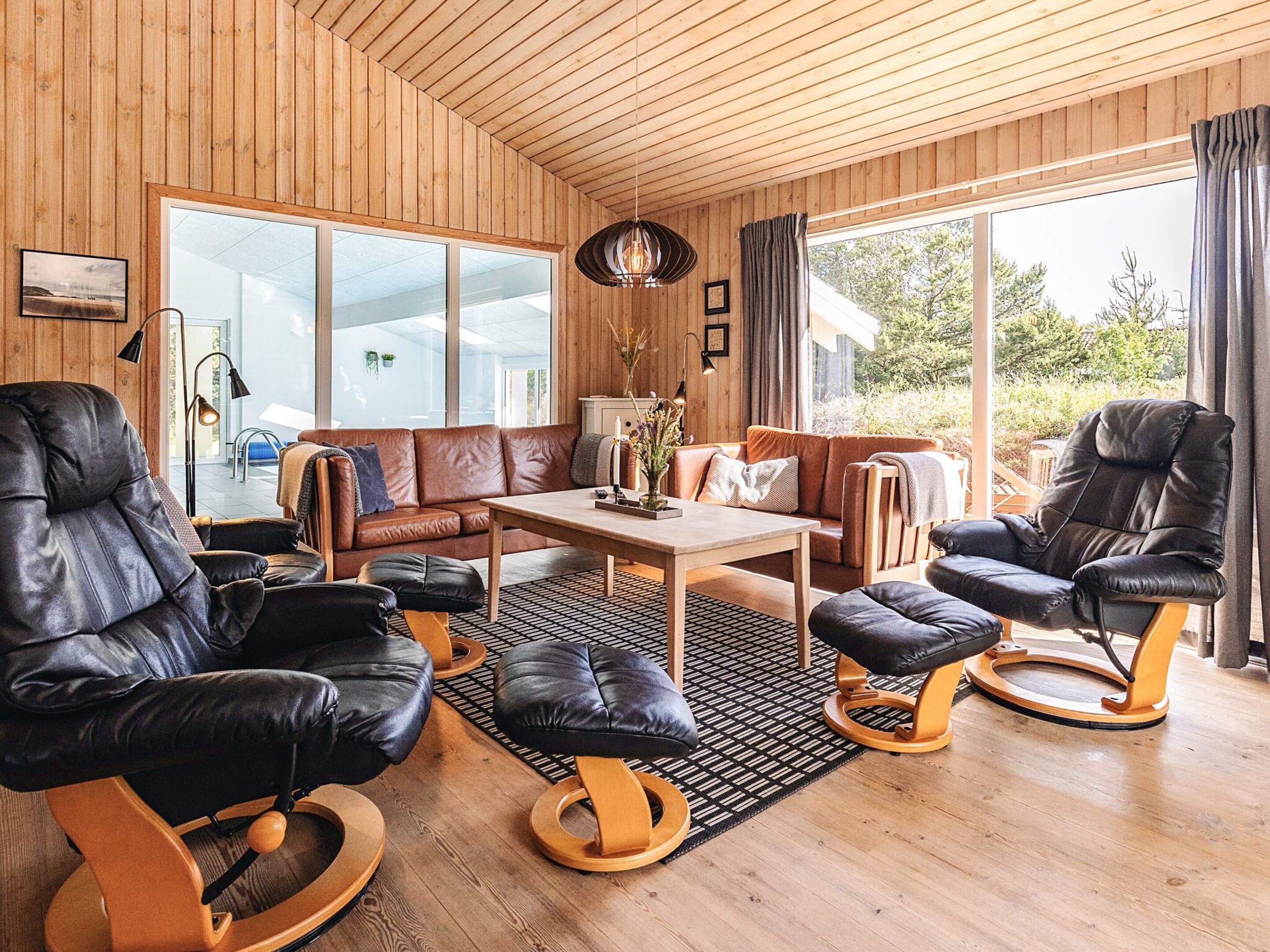 A modern living room with leather sofas, a wooden coffee table, and a large window offering a view of the outdoors.