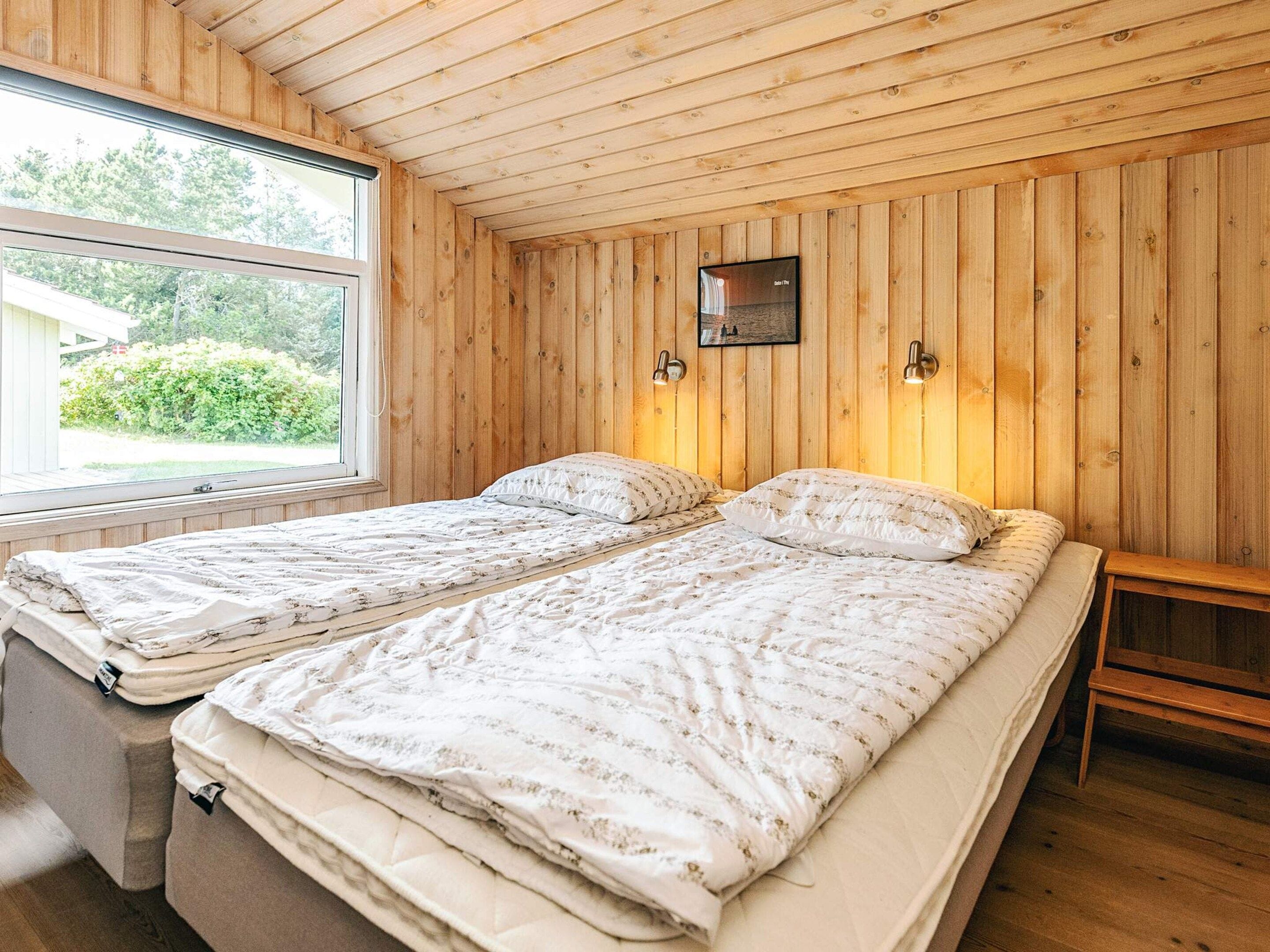 A room with two beds, wooden walls, a window, and a small table.