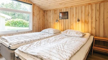 A room with two beds, wooden walls, a window, and a small table.