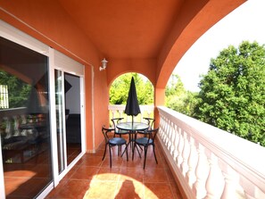 Uma varanda com porta de vidro, mesa redonda com cadeiras e um guarda-sol preto.