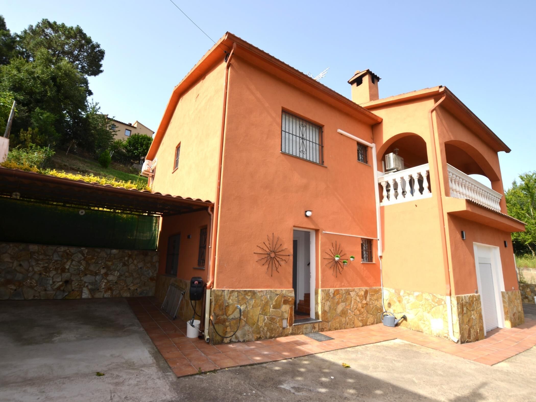 A two-story house with a stone foundation, a balcony, and a small garden area.