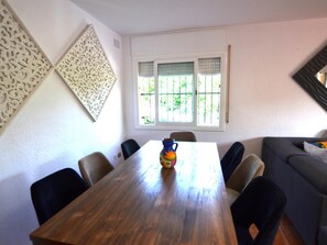 Uma sala de jantar com uma mesa de madeira, cadeiras, um painel decorativo na parede e uma janela com grades.