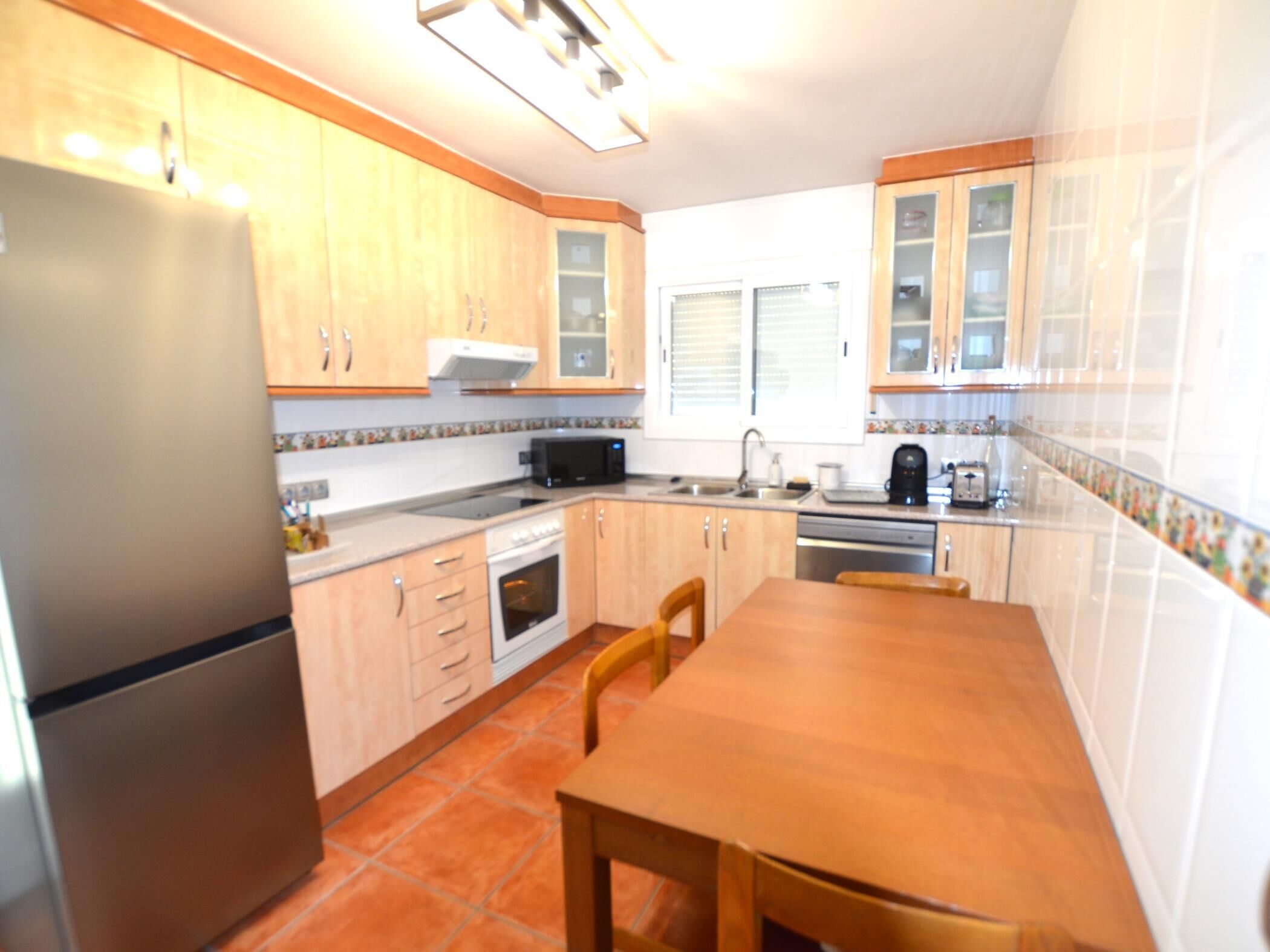 A kitchen with wooden cabinets, a refrigerator, a microwave, and a dining table with chairs.