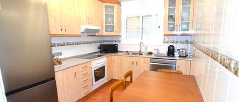 A kitchen with wooden cabinets, a refrigerator, a microwave, and a dining table with chairs.