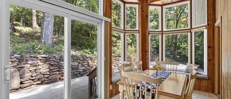Un interior de madera con una pared de piedra en el exterior, una mesa de comedor con sillas y ventanas amplias.