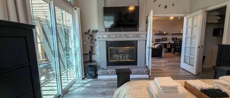 A spacious room with a large bed, a fireplace, a television, and a view through large windows.