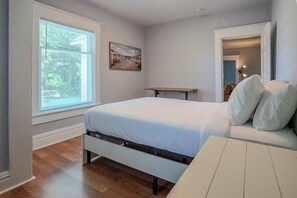 Un dormitorio con cama, ventana, cuadro y puerta que da a otra habitación.