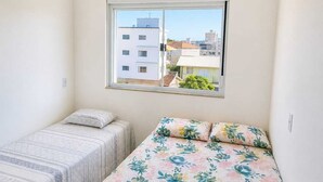 Een slaapkamer met twee bedden, een raam met uitzicht op gebouwen, en een effen muur.