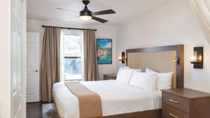 A hotel room with a bed, a ceiling fan, a nightstand, a lamp, a painting, and a view of the outdoors. - Two bedroom deluxe resort at West flamingo Bay resort Las Vegas (Las Vegas)
